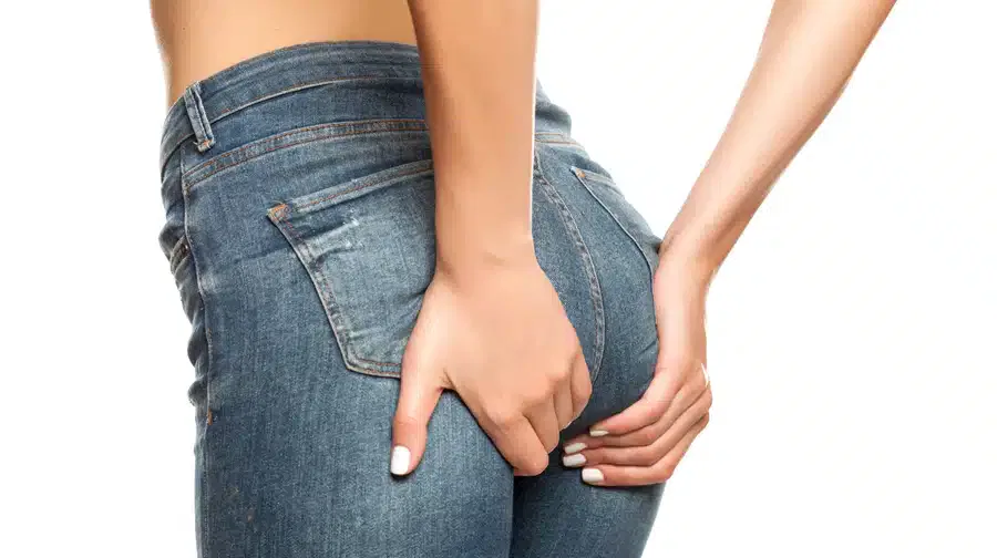 A woman in jeans holding her hand to her back, experiencing discomfort or pain.