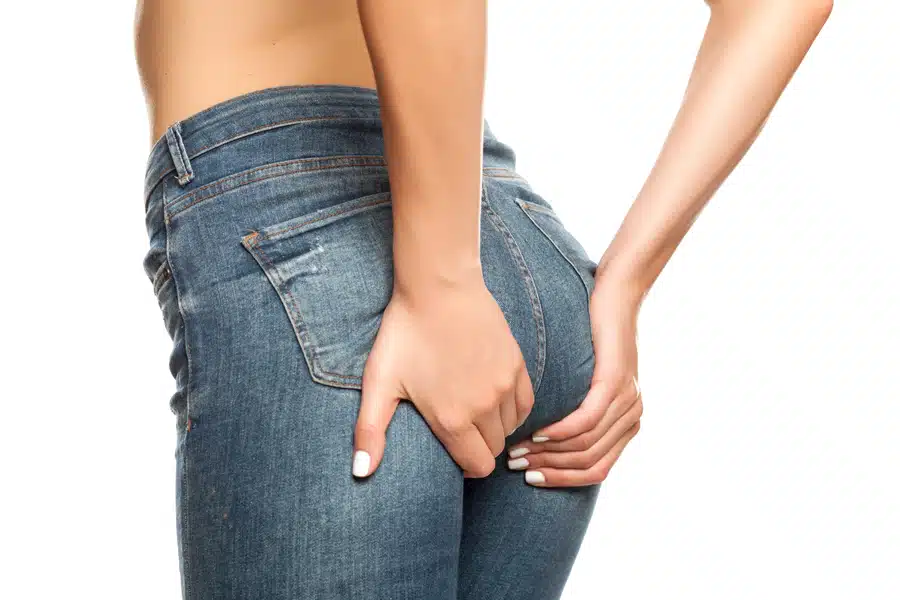 A woman in jeans holding her hand to her back, experiencing discomfort or pain.