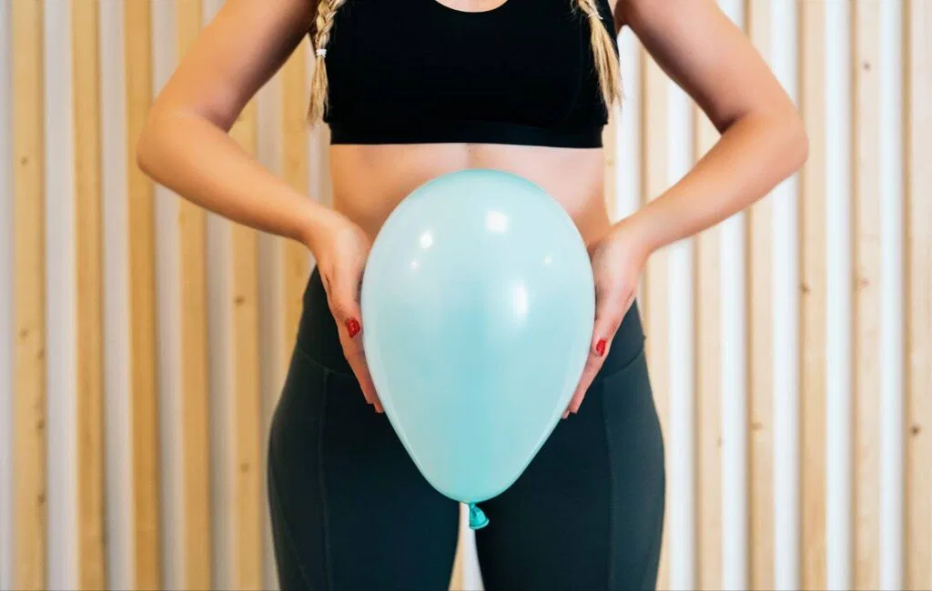 A woman wearing a sports bra top joyfully holds a blue balloon set against a vibrant backdrop