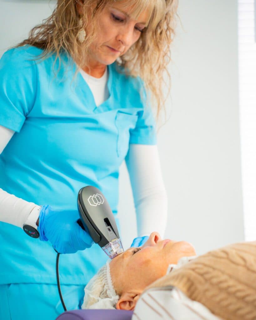 A woman in a blue shirt uses a device to provide treatment to an elderly woman at Ivee Restorative Care.