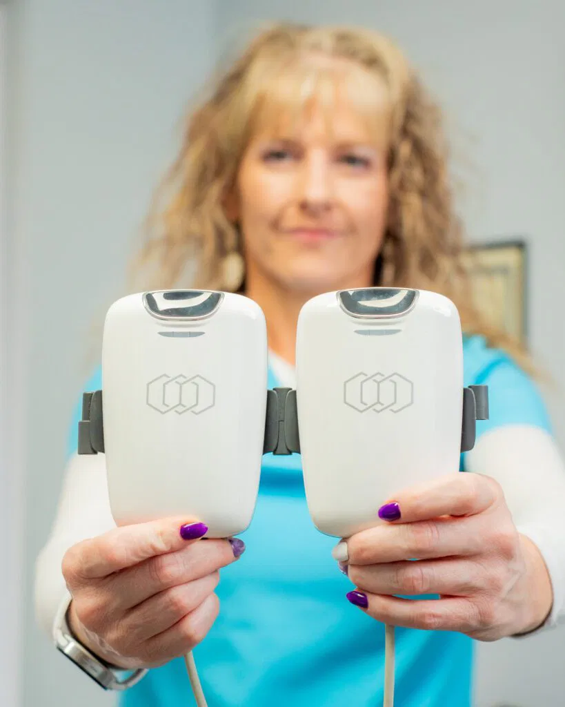 A woman wearing a blue shirt is holding two electronic devices, showcasing the innovative tools from Ivee Restorative Care.