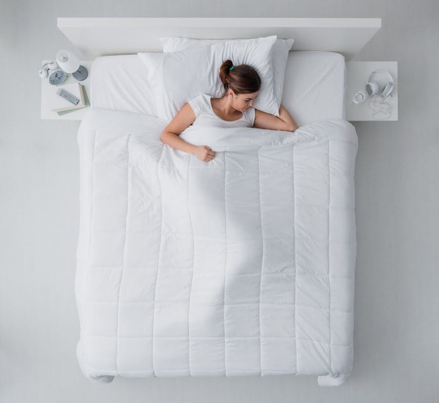 A woman peacefully sleeps in a bed covered with a white comforter, symbolizing mental health and relaxation.